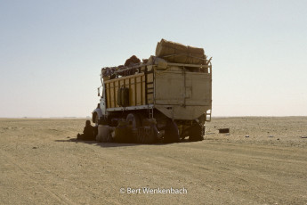 Passengers shelter from the sun in the shade of the truck, while the driver is fixing it